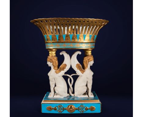 Glazed and gilded ceramic. Dimensions: 56 x 49 x 28 cm. This imposing centrepiece, supported by two winged sphinxes, combines