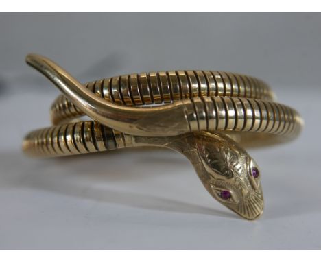 A Victorian style vintage 9ct gold sprung snake bangle (Expands). The snake's head engraved foliate and scale design, the eye