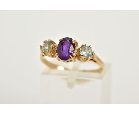A 9CT GOLD AMETHYST AND TOPAZ RING, designed with a central claw set oval cut amethyst, flanked with claw set circular cut bl
