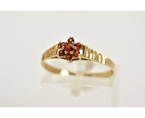 A 9CT GOLD GARNET CLUSTER RING, designed with a small central cluster set with seven circular cut garnets, textured shoulders