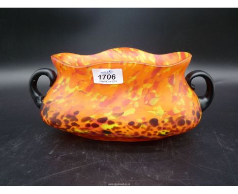 An orange vintage Czech Spatter glass bowl with random colour splashes and having two black handles, 5" tall, 11" wide.