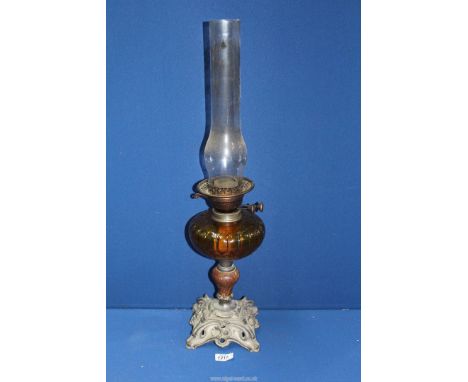 An oil lamp with ornate floral cast metal base, stone column and an amber glass reservoir, 25 3/4'' tall overall with chimney