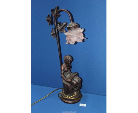 A table lamp with a resin figure of a  Lady reading at the base and leaves to the top fitted with a pink frosted glass lamp s