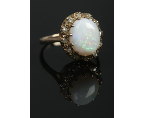 A 9ct gold dress ring set with a large cabochon opal stone within a diamond halo surround. Hallmarks for London 1975. Size P 