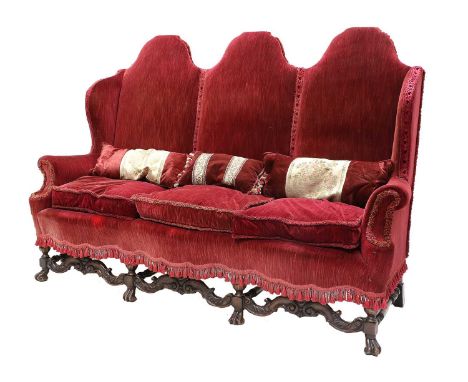 A William &amp; Mary-Style Three-Seater Wing-Back Sofa, early 20th century, covered in red velvet, with three squab cushions 