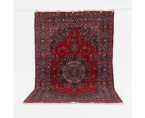 A red-ground wool carpet,  20th century, Kirman style, with a shaped central medallion within a sparsely decorated floral fie