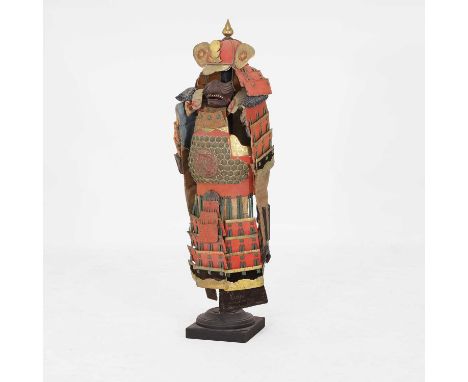 A small model Samurai armour display, 20th century, Japanese, decorated in tones of red, green and gilt, raised on an ebonise