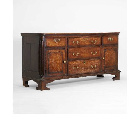 A George III oak dresser base, c.1780, having a central bank of three drawers, flanked by shaped cupboard doors and stop-flut