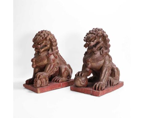 A pair of gilt-lacquered wood carvings, 20th century, Chinese, each of a Buddhist lion, seated on its haunches, with bulging 
