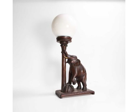 A carved table lamp, c.1900, Anglo-Indian, modelled as an elephant with its trunk curled around the column, fitted with a whi