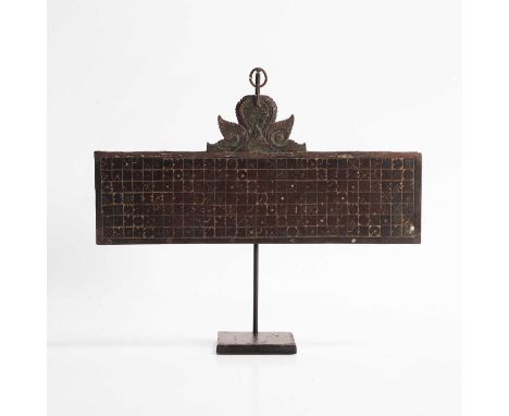 A carved wood calendar, 19th century, Indonesian, the rectangular panel with a curved pediment above, mounted on a later stan
