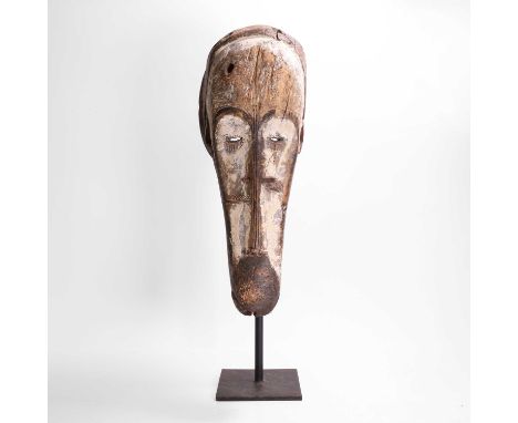 A painted Ngil-type mask, 20th century, Gabon, Fang people, with a peg through the nose and pouting mouth, raised on a metal 