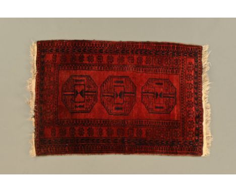 An Eastern fringed rug, dark red and blue with centre rectangular panel with three similar designs and with multiple line bor