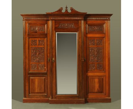 A Victorian walnut triple wardrobe, carved throughout with scrolled leafage motifs, the central section enclosed by a bevelle