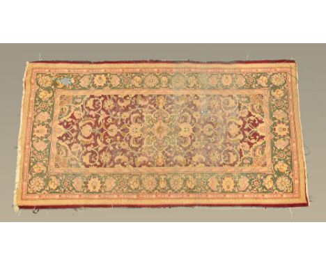 A rectangular fringed carpet, with green foliate patterned border and centre rectangular panel also foliate patterned, princi