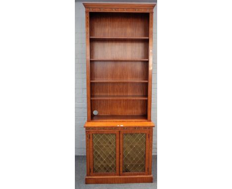 A 20th century floral polychrome painted satinwood bookcase/ cabinet, the open four tier shelf back over a pair of brass gril