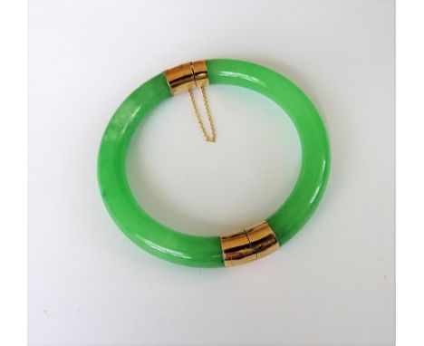 A circular treated jade hinged bangle, on a snap clasp, fitted with a safety chain.