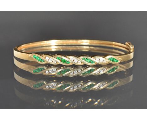 A gold, emerald and diamond set oval hinged bangle, the front mounted with three rows of three circular cut diamonds, alterna