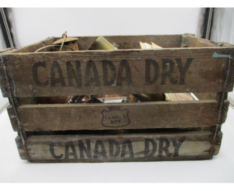 A collection of miscellaneous items in a vintage Canada Dry advertising crate, including a miners lamp, copper jug etc