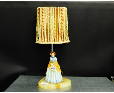 A table lamp, the hardstone base surmounted by a Royal Doulton style figure wearing and blue dress and orange shawl carrying 