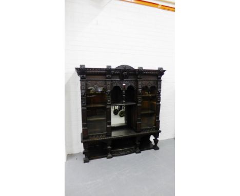 A carved oak cabinet, the dentil cornice with a mask head emblem to centre above a central mirror back alcove, flanked by a p