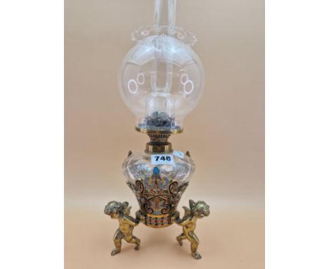 A LATE 19th C. FRENCH CLEAR CUT GLASS AND CHAMPLEVE ENAMEL OIL LAMP SUPPORTED BY THREE BRASS CUPIDS