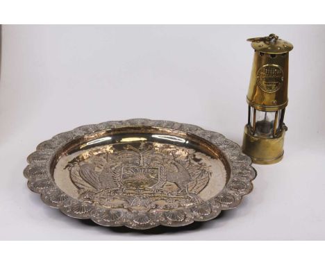 A plated metal charger, the well repousse decorated with a crest and Latin motto, the rim repousse decorated with scallop she