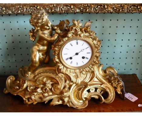 A gilt metal rococo-style striking mantle clock, featuring a cherub above scrolled and floral base, the face with Roman numer