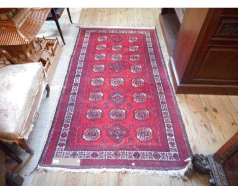 A woollen carpet with geometric designs on a red ground, surrounded by white and red geometric border, 76 x 108cm.