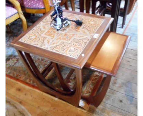 A 1970's set of three teak G-plan nesting tables, the largest with four tile decoration, each on stylized supports, the large