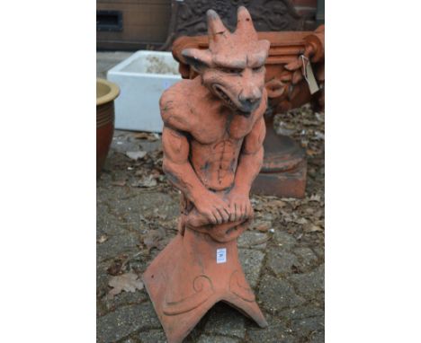 A terracotta coloured garden ornament modelled as a gargoyle on a ridge tile.