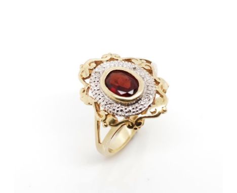 Garnet and 9ct yellow gold ring with a white gold highlighted halo set with diamond chips. Marked 9ct. Approx weight 3.2 gram