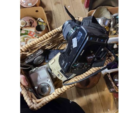A basket containing cameras including a Pentax K20, a Fijifilm compact camera, etc.