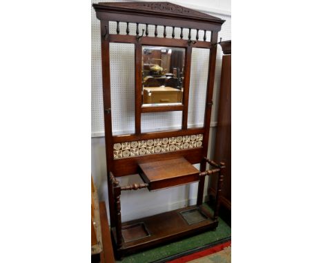 A late Victorian oak hallstand, architectural pediment, spindled back over rectangular plate, tile back above glove box, turn