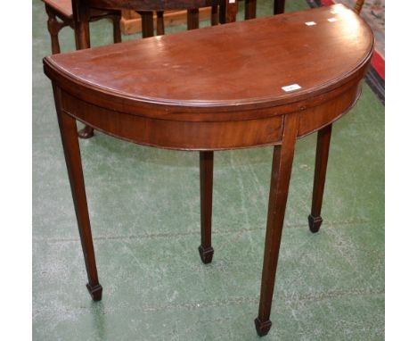 An Edwardian mahogany demi-lune card table, the top opening to green baize playing surface, tapering square legs, spade feet.