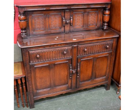 An Ercol court cupboard, two carved panel doors flanked by cup and cover pilasters to top, two fluted front drawers over two 