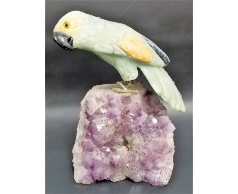 Interesting hard stone model of a parrot with glass inset eyes upon an amethyst specimen boulder, height 9.25'