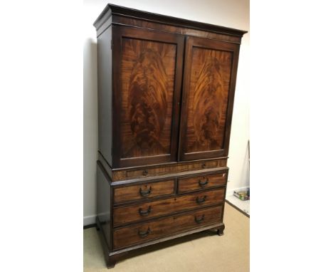 A late George III mahogany linen press, the moulded cornice over two oval figured panelled doors, opening to reveal a hanging