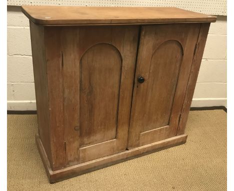 A Victorian pine two door cupboard, the domed panelled doors enclosing two shelves on a plinth base, 107 cm wide x 42 cm deep