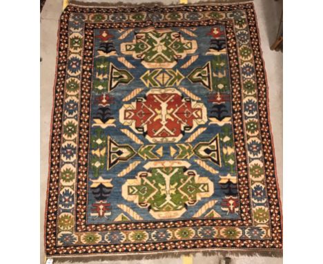 A Caucasian rug, the central panel set with three repeating medallions on a pale blue ground, within a geometric patterned st