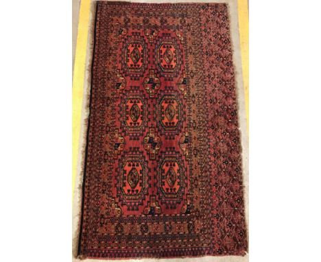 A Bokhara tribal rug, the main panel set with repeating elephant foot style medallions on a red ground within a red and black