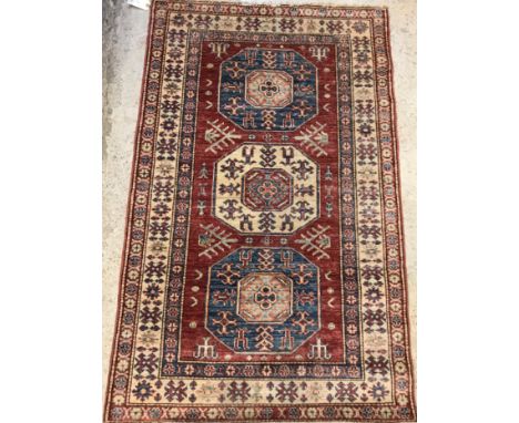 A modern Persian rug, the central panel set with three repeating medallions on a red ground, within a stepped blue, red and c