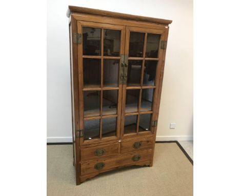 A 20th Century Chinese elm display cabinet with two glazed doors over two short and one long drawer on a bracket foot base, 1