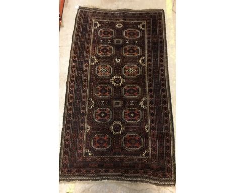 A Belouch tribal rug, the central panel set with repeating elephant foot style medallions on a dark aubergine ground, within 