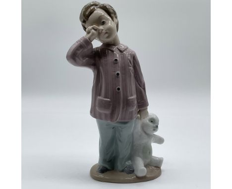 This charming Nao by Lladro porcelain figurine, titled Sleepy Head, showcases a young child holding a plush teddy bear, dress