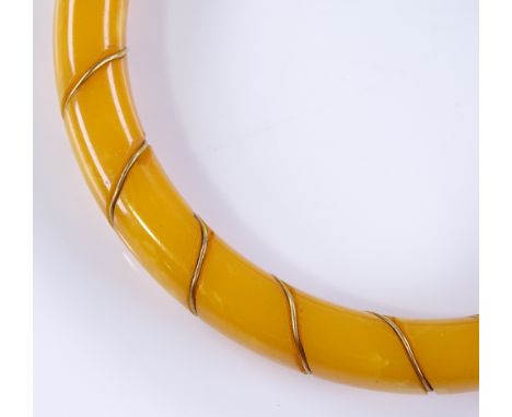 A butterscotch amber bangle, carved and inlaid with gilt-metal wire, internal diameter 63.6mm, 18.6g