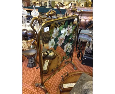 An Art Nouveau brass framed mirrored fire screen with painted floral decoration.