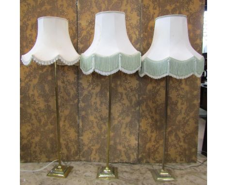 A set of three brass column lamp standards on square cut bases, together with three industrial green enamelled lamp shades 