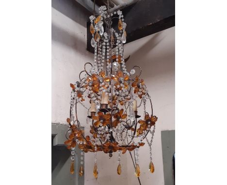An open scrolling light metal hanging ceiling light with floral detail, trailing prism swags and tinted amber coloured prism 