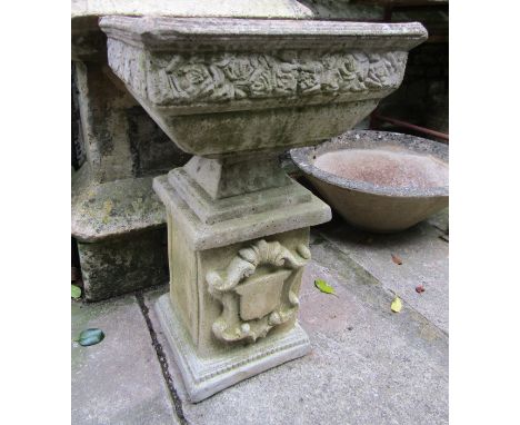 A weathered cast composition stone garden urn of square tapered form with rose relief collar raised on a loose socle and squa